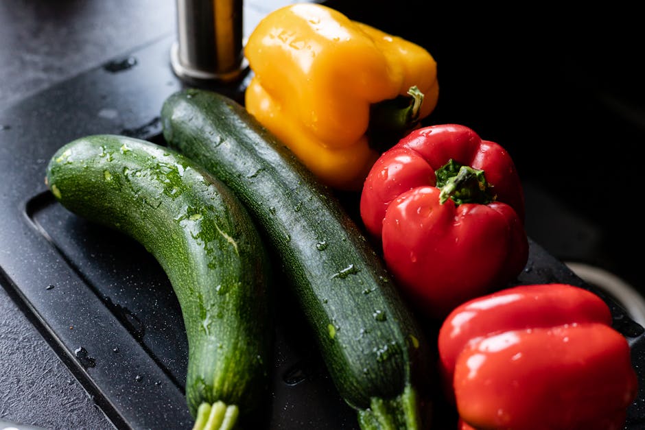 Vibrant bell peppers and zucchinis on a damp, dark surface.